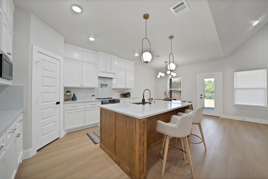 Kitchen with brown cabinets, light wood finished floors, a kitchen island with sink, white cabinetry, and recessed lighting Kitchen with brown cabinets, light wood finished floors, a kitchen island with sink, white cabinetry, and recessed lighting