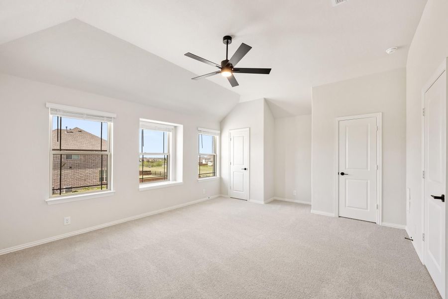 Empty bedroom with vaulted ceiling, ceiling fan, carpet flooring, and three windows Empty bedroom with vaulted ceiling, ceiling fan, carpet flooring, and three windows