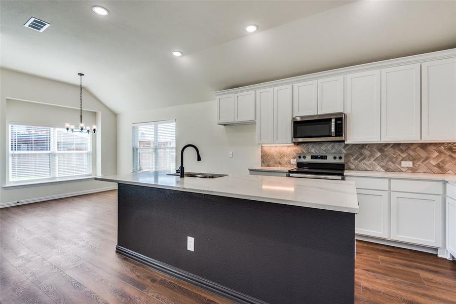 Kitchen featuring appliances with stainless steel finishes, lofted ceiling, dark hardwood / wood-style floors, and an island with sink