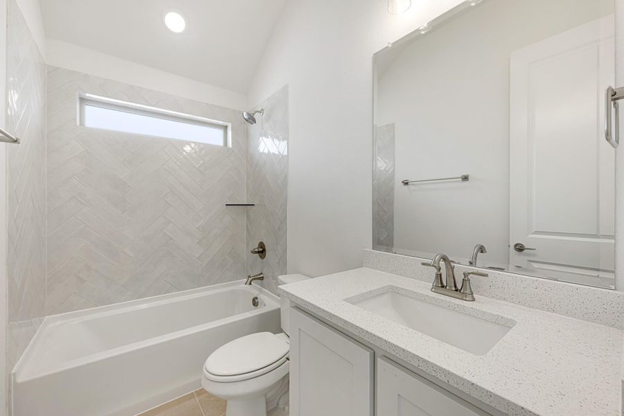 Bathroom with herringbone tile tub surround, white vanity with quartz countertop, and vaulted ceiling Bathroom with herringbone tile tub surround, white vanity with quartz countertop, and vaulted ceiling
