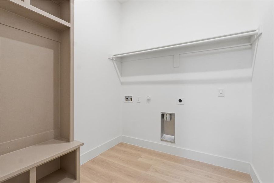 Laundry area featuring a built-in shelving unit, coordinating bench with storage, overhead shelving, and wood-finish flooring Laundry area featuring a built-in shelving unit, coordinating bench with storage, overhead shelving, and wood-finish flooring