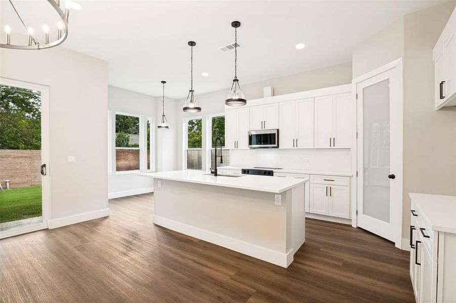 Contemporary kitchen featuring white cabinetry, a large center island with a sink, stainless steel appliances, and wood-finish flooring