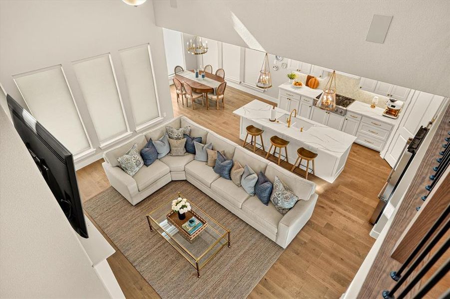Open-concept living space featuring high ceilings, wood-finish flooring, a kitchen island with seating, white cabinetry, and a dining area with chandelier lighting Open-concept living space featuring high ceilings, wood-finish flooring, a kitchen island with seating, white cabinetry, and a dining area with chandelier lighting