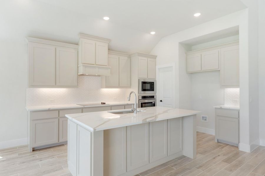White kitchen with center island, quartz countertops, stainless steel appliances, and light wood-look tile floors
