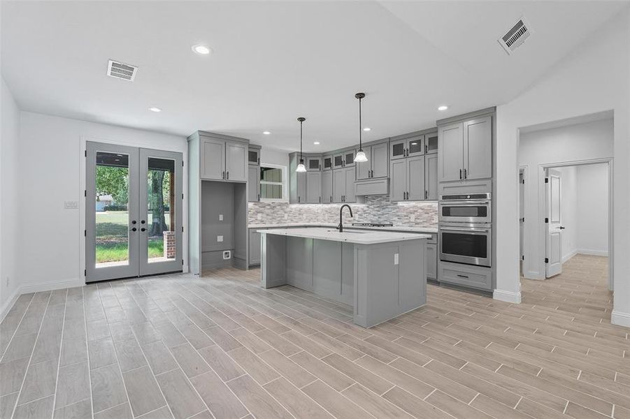 Kitchen featuring gray cabinetry, backsplash, french doors, a center island with sink, and recessed lighting Kitchen featuring gray cabinetry, backsplash, french doors, a center island with sink, and recessed lighting