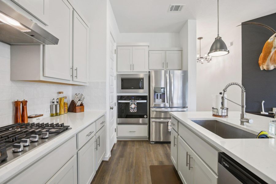 Kitchen with white cabinetry, under cabinet range hood, appliances with stainless steel finishes, pendant lighting, and backsplash Kitchen with white cabinetry, under cabinet range hood, appliances with stainless steel finishes, pendant lighting, and backsplash