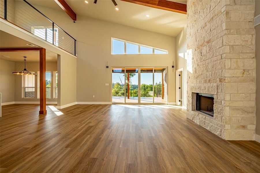 Unfurnished living room with beamed ceiling, a stone fireplace, wood finished floors, a towering ceiling, and recessed lighting Unfurnished living room with beamed ceiling, a stone fireplace, wood finished floors, a towering ceiling, and recessed lighting