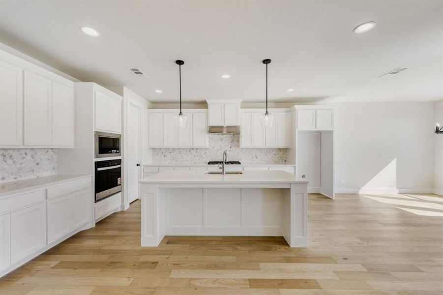 Kitchen with white cabinets, light wood-style flooring, pendant lighting, and stainless steel appliances