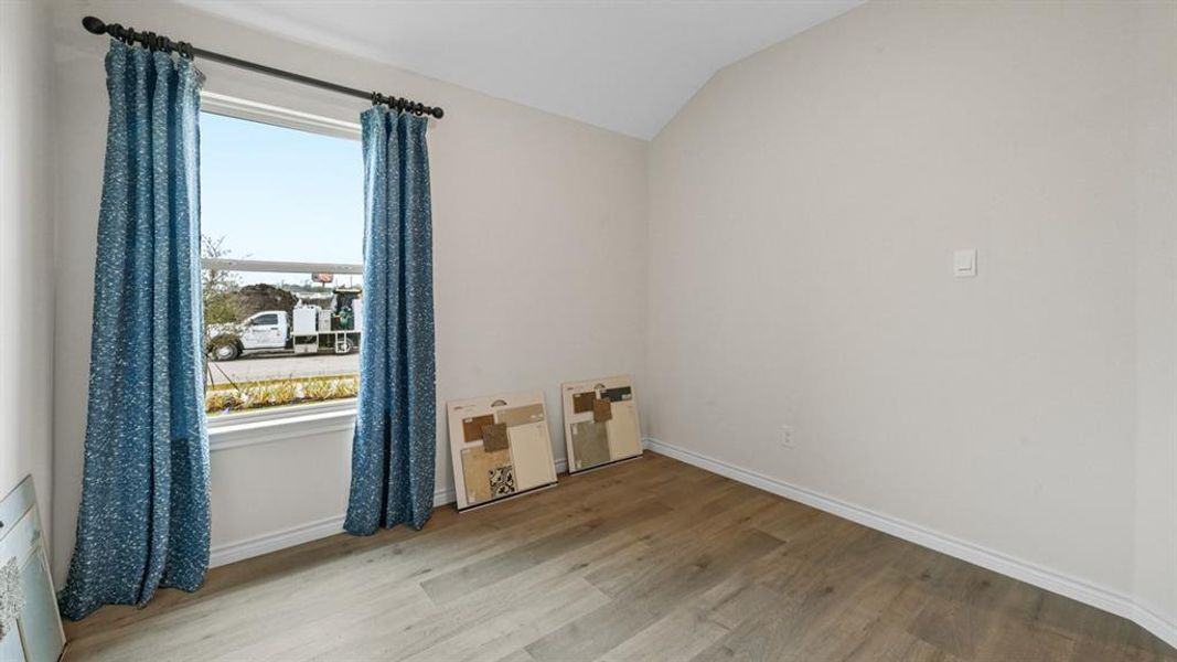 Unfurnished room with light wood-style floors and lofted ceiling Unfurnished room with light wood-style floors and lofted ceiling