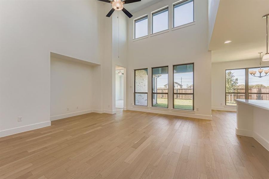 Unfurnished living room with light wood finished floors, a towering ceiling, a ceiling fan, and recessed lighting Unfurnished living room with light wood finished floors, a towering ceiling, a ceiling fan, and recessed lighting
