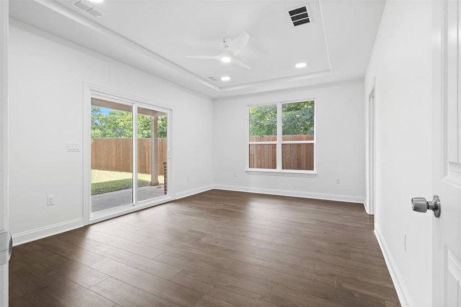 Unfurnished room with healthy amount of natural light, dark wood-style floors, a ceiling fan, a tray ceiling, and recessed lighting
