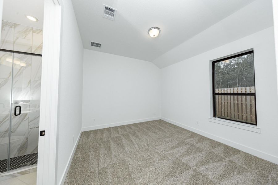 This inviting secondary bedroom combines comfort and modern elegance, featuring sloped ceiling, plush carpeting, a neutral color palette, abundant natural light streaming through a large window, a walk-in closet, and an ensuite secondary bathroom.