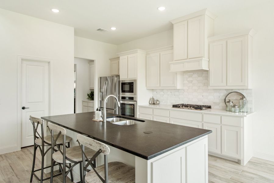 Kitchen with white cabinets, dark island with seating, stainless steel appliances, and tile backsplash Kitchen with white cabinets, dark island with seating, stainless steel appliances, and tile backsplash