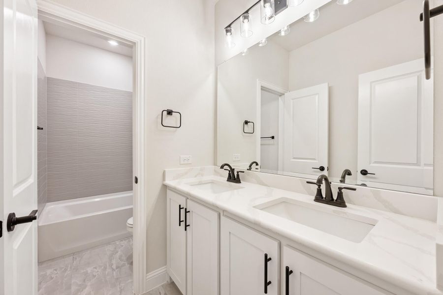 Bathroom with double sink vanity, white cabinets, quartz countertops, and tub-shower combo with gray tile Bathroom with double sink vanity, white cabinets, quartz countertops, and tub-shower combo with gray tile