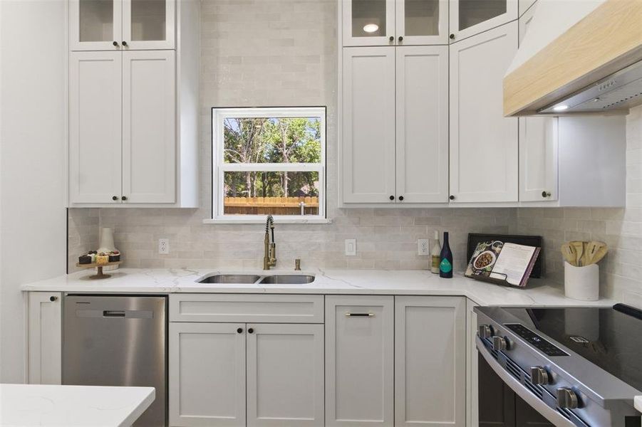 Modern kitchen featuring white shaker cabinetry, stainless steel appliances, a double basin sink with an arched faucet, light-toned tile backsplash, and light-colored countertops
