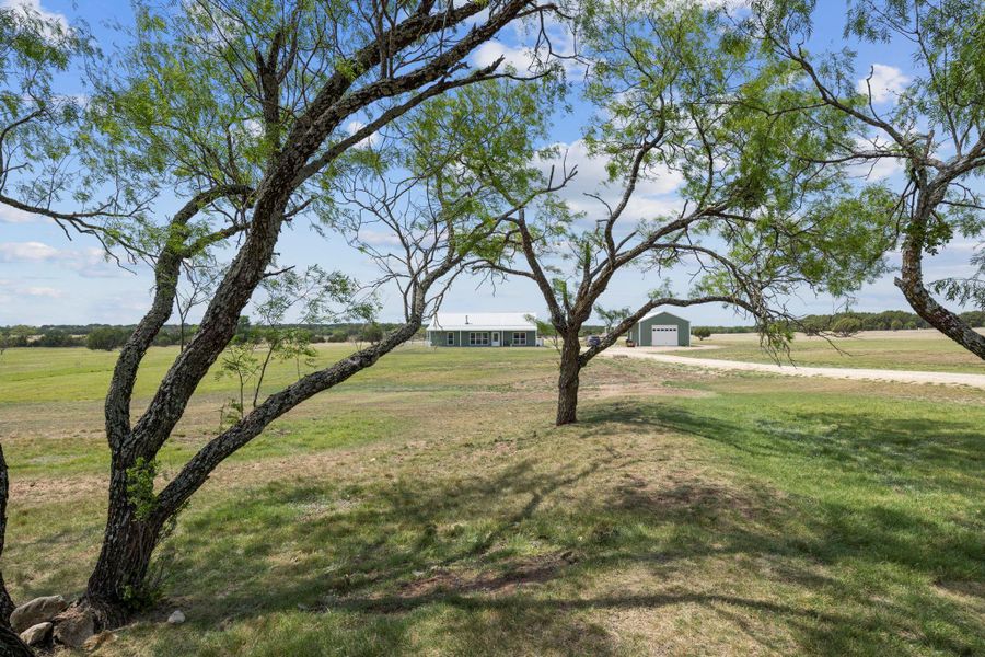 View of grassy yard with dirt driveway, a detached garage, a view of rural / pastoral area, and an outbuilding