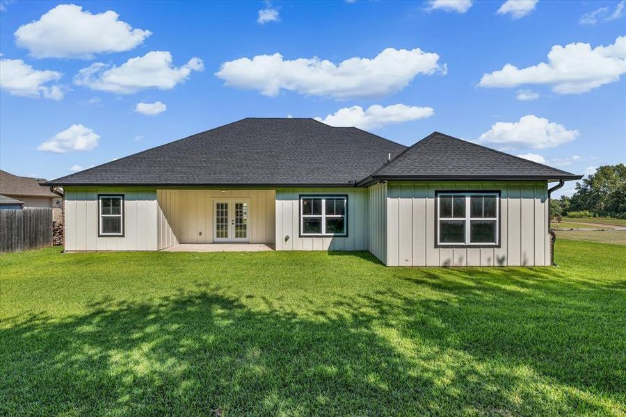 Rear view of property featuring a yard, a patio, roof with shingles, french doors, and board and batten siding Rear view of property featuring a yard, a patio, roof with shingles, french doors, and board and batten siding