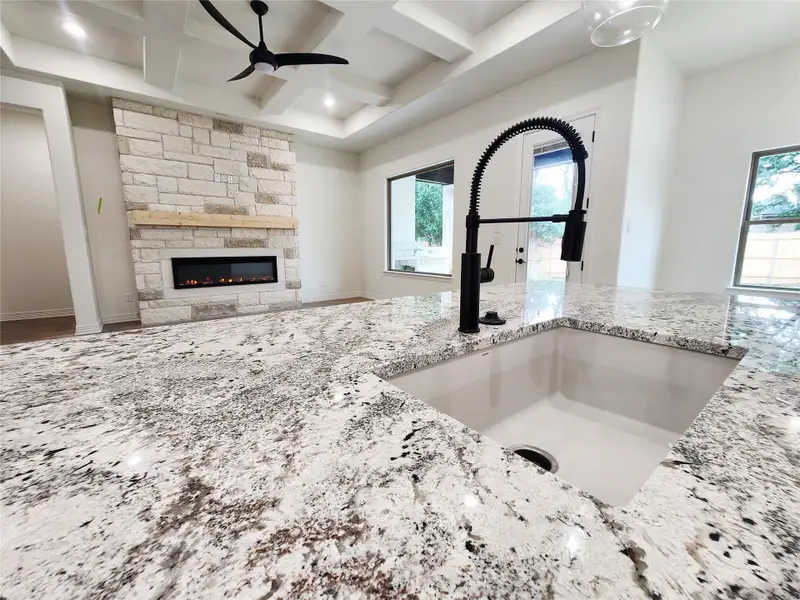 Kitchen island featuring light-toned granite countertops and an undermount sink with a matte black gooseneck faucet