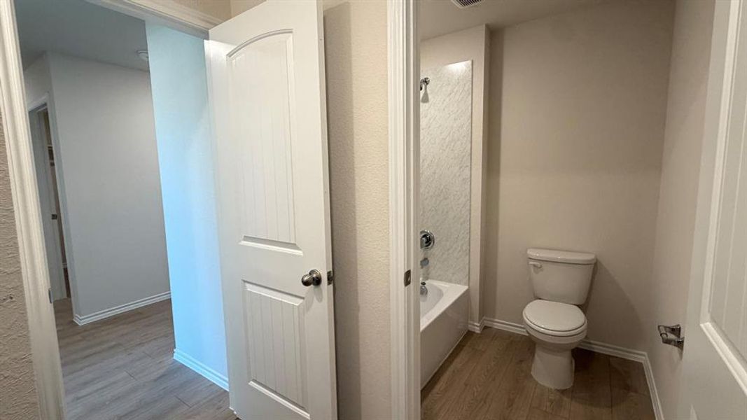 Full bathroom featuring a white tub/shower combination with a textured wall surround, a white toilet, and wood-finish flooring
