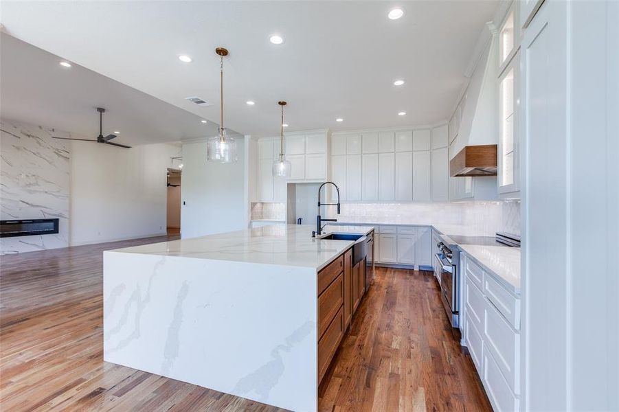 Kitchen featuring light hardwood / wood-style floors, white cabinetry, light stone counters, ceiling fan, and a large island