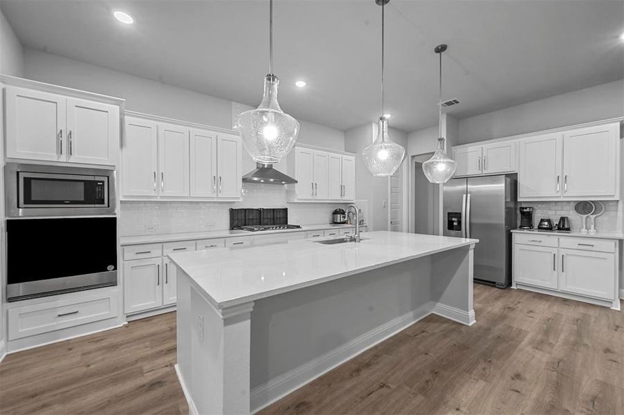 Kitchen with backsplash, stainless steel appliances, white cabinetry, and light wood flooring