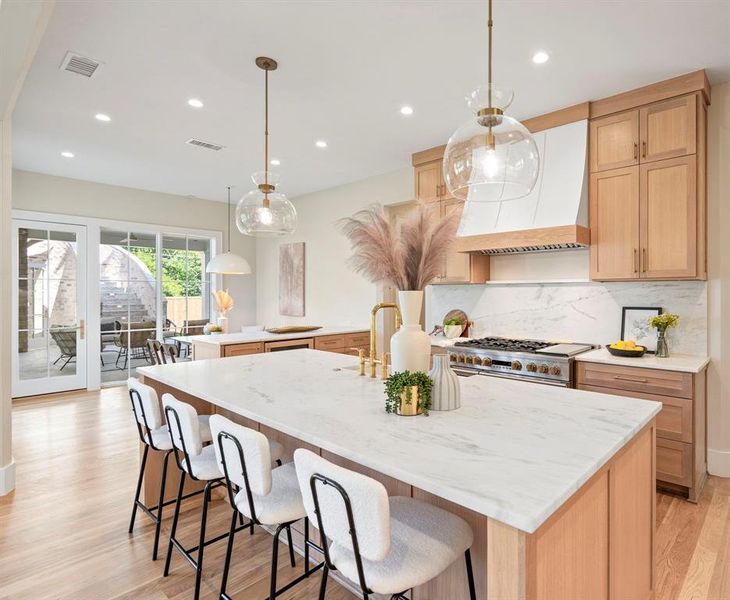 Kitchen featuring backsplash, light hardwood / wood-style floors, a center island with sink, and custom range hood