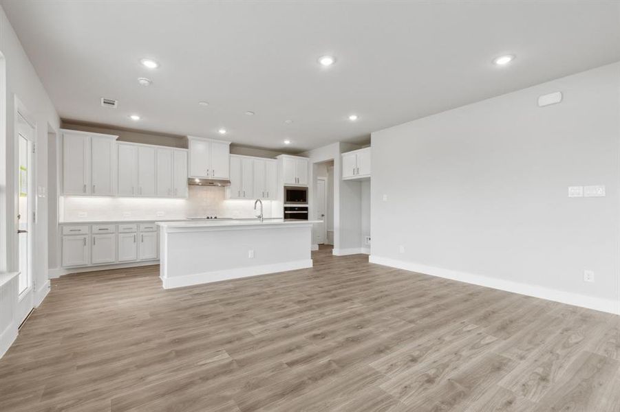 Kitchen featuring stainless steel microwave, under cabinet range hood, oven, backsplash, and white cabinets Kitchen featuring stainless steel microwave, under cabinet range hood, oven, backsplash, and white cabinets