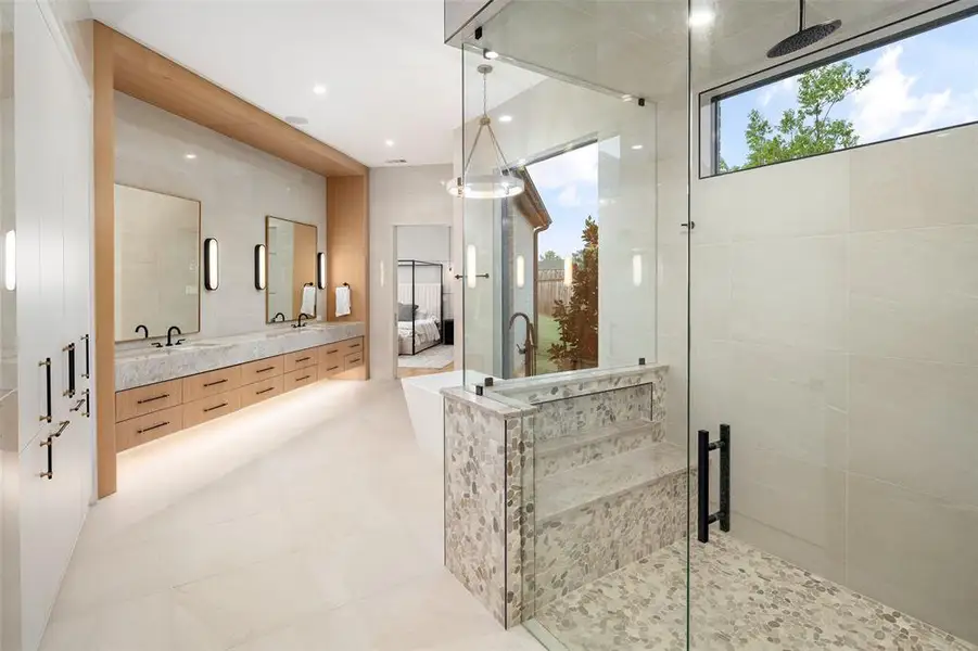 Oversized walk-in shower featuring upgraded tile, frameless glass enclosure, and elegant designer fixtures. The spa-like design blends beautifully with the luxurious finishes throughout the primary bathroom, creating a bright and sophisticated retreat.