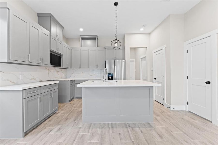 This modern kitchen features sleek gray cabinets, a large central island with a quartz countertop, stainless steel appliances, and stylish light fixtures. The space is bright and open, with wood-look flooring and ample storage.