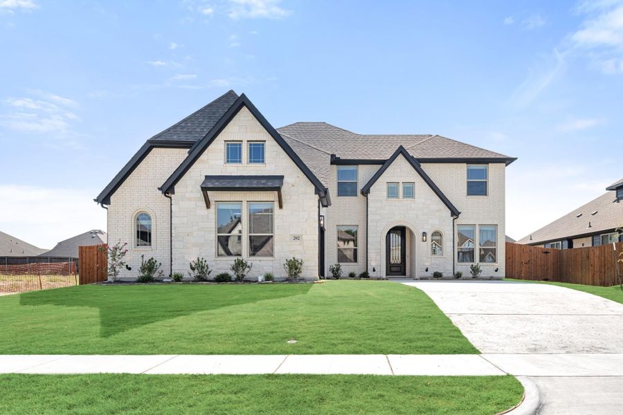 Two-story home with cream brick exterior, arched entry door, dark trim, and manicured front lawn with concrete driveway Two-story home with cream brick exterior, arched entry door, dark trim, and manicured front lawn with concrete driveway