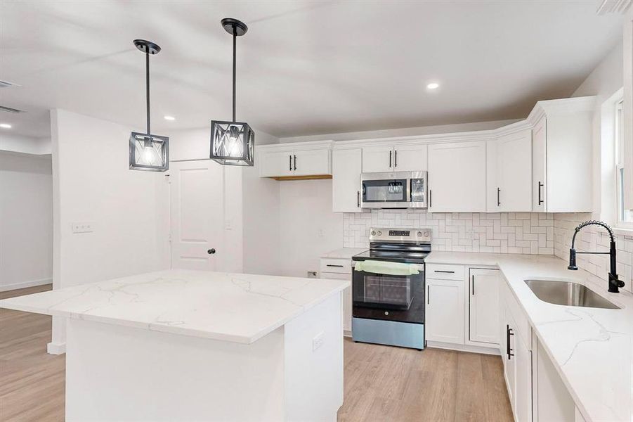 Kitchen with appliances with stainless steel finishes, sink, a center island, light hardwood / wood-style floors, and white cabinetry