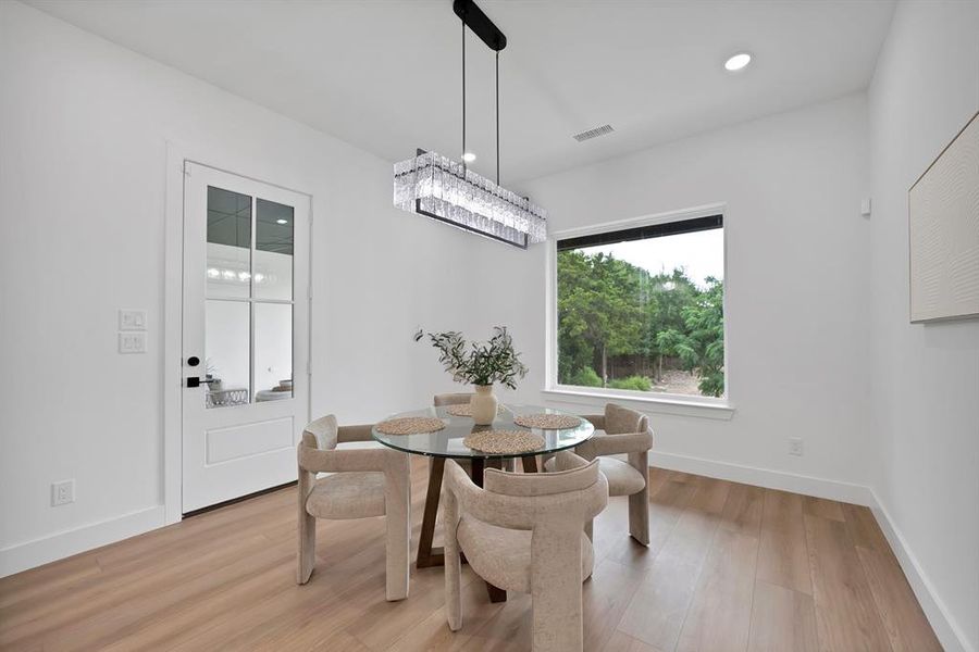 Dining space featuring wood-finish flooring, a contemporary rectangular chandelier, a large picture window, a white paneled door with glass inserts, and recessed lighting