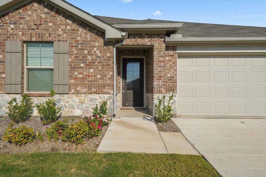 Property entrance with brick siding, a garage, roof with shingles, and concrete driveway Property entrance with brick siding, a garage, roof with shingles, and concrete driveway
