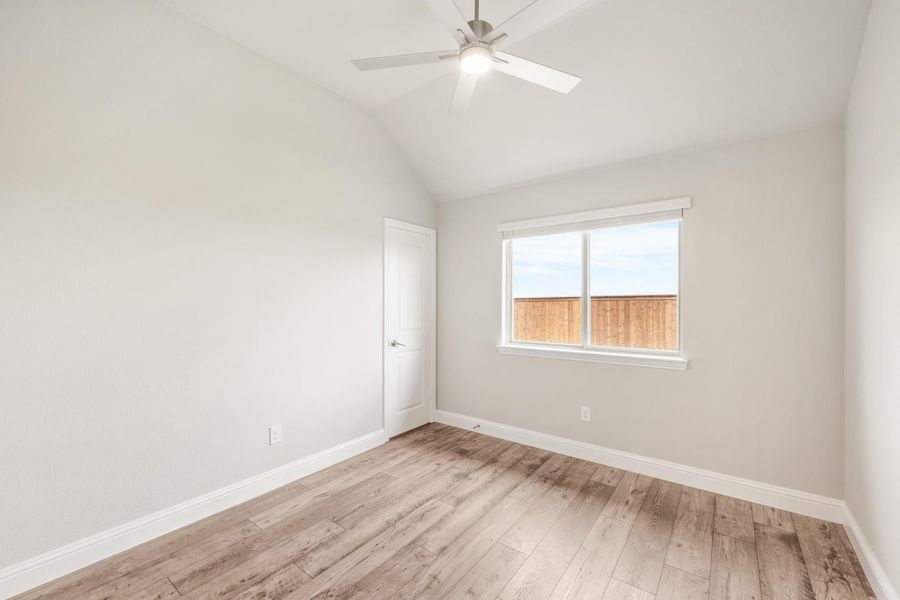 Empty bedroom with vaulted ceiling, ceiling fan, wood-look floors, and single window with backyard view. Empty bedroom with vaulted ceiling, ceiling fan, wood-look floors, and single window with backyard view.