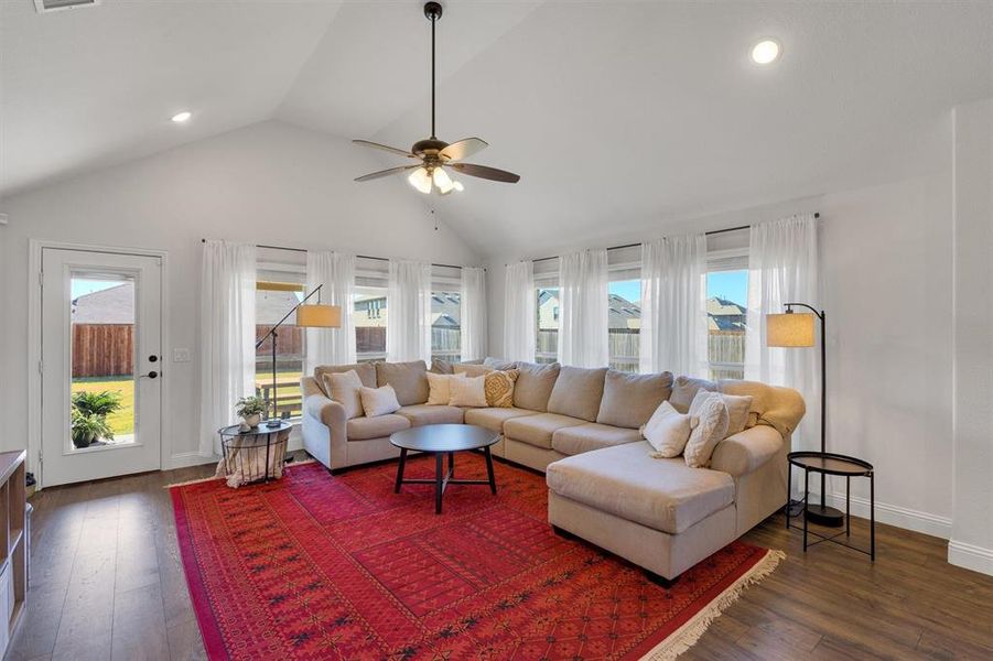 Living room with dark hardwood / wood-style floors, high vaulted ceiling, plenty of natural light, and ceiling fan