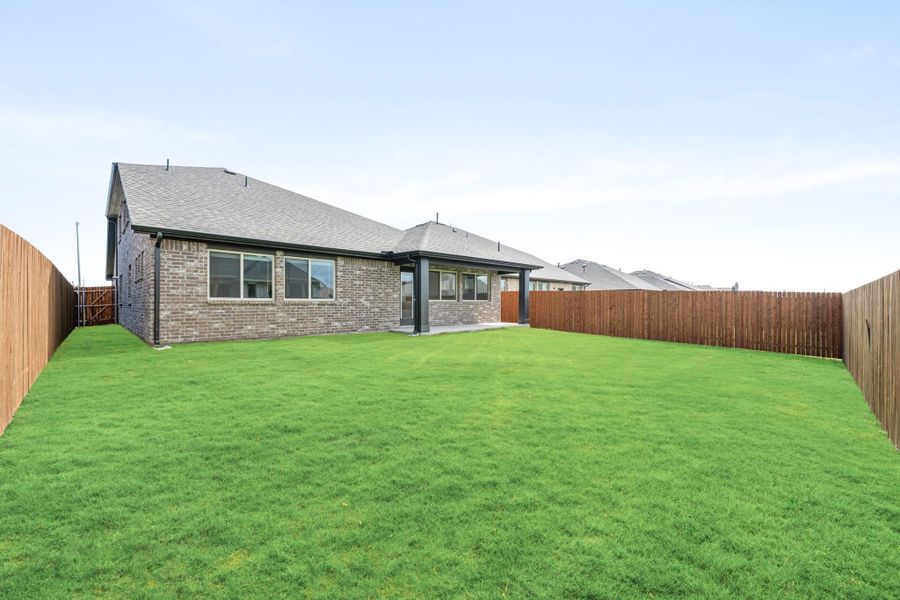 Brick home rear exterior with covered patio, large green lawn, and wood privacy fence