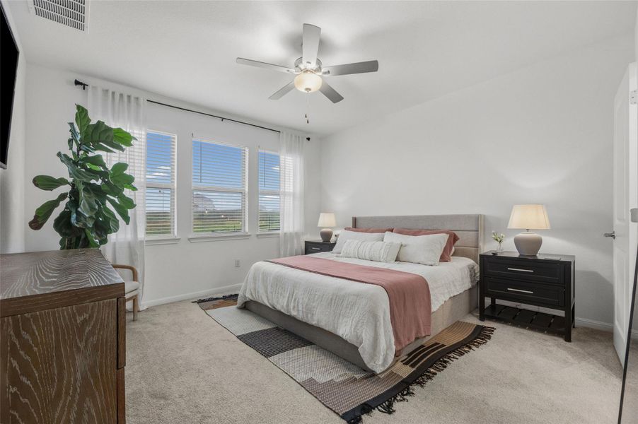 Carpeted bedroom featuring white walls, a ceiling fan with integrated lighting, and a series of three large windows providing abundant natural light