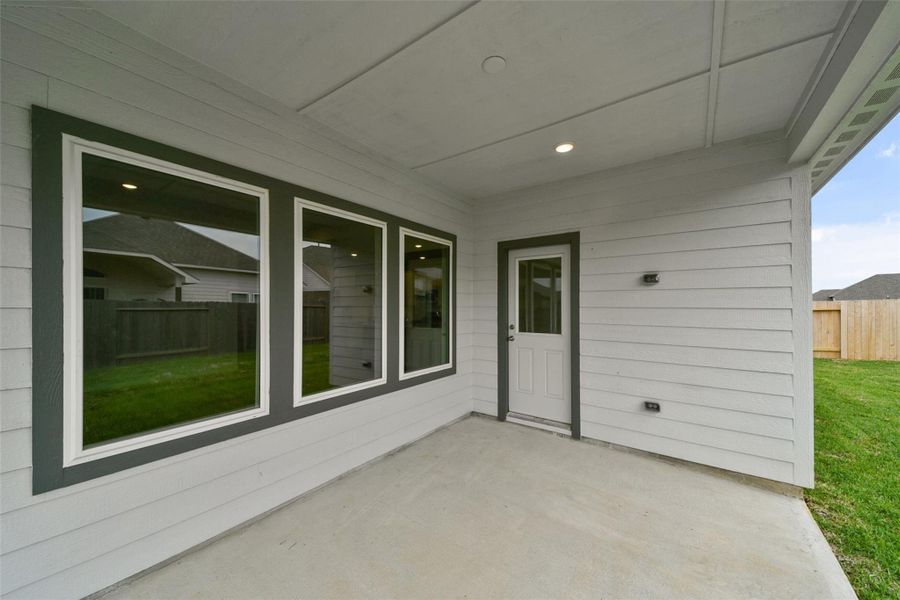 Cozy covered patio featuring light gray siding, large windows, and direct access to a grassy backyard—perfect for relaxing or entertaining.