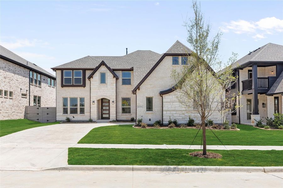 Two-story home with light stone exterior, arched entry, and concrete driveway on a green lawn