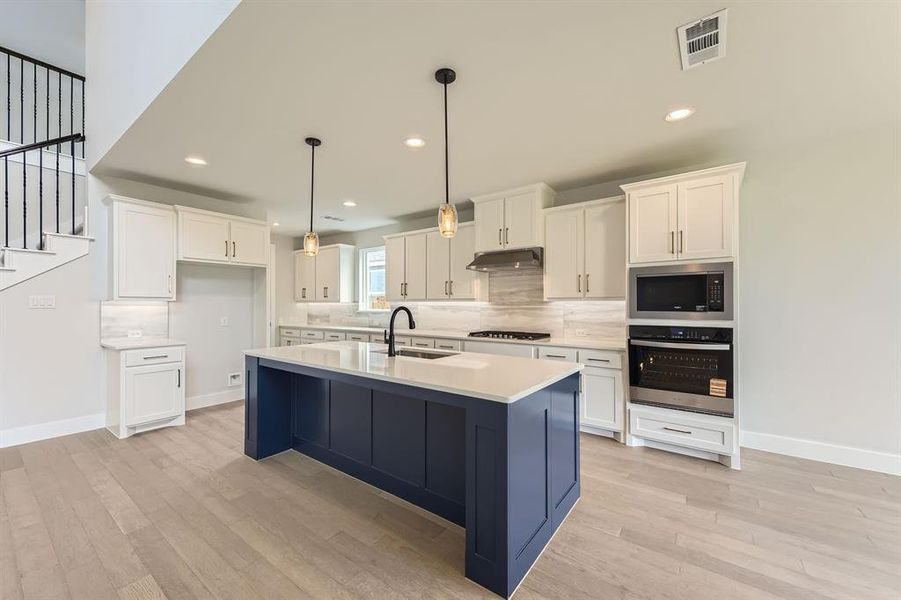 Kitchen with appliances with stainless steel finishes, under cabinet range hood, a sink, light wood-style floors, and white cabinets