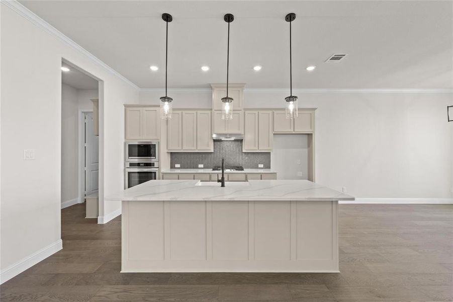 Kitchen with a kitchen island with sink, light stone countertops, and pendant lighting