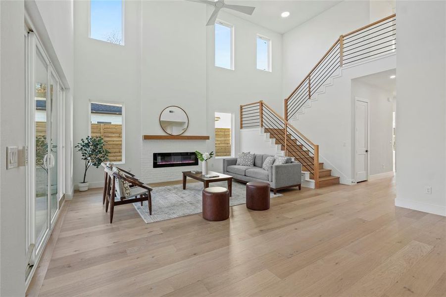 Living room featuring stairway, light wood finished floors, a glass covered fireplace, a towering ceiling, and recessed lighting