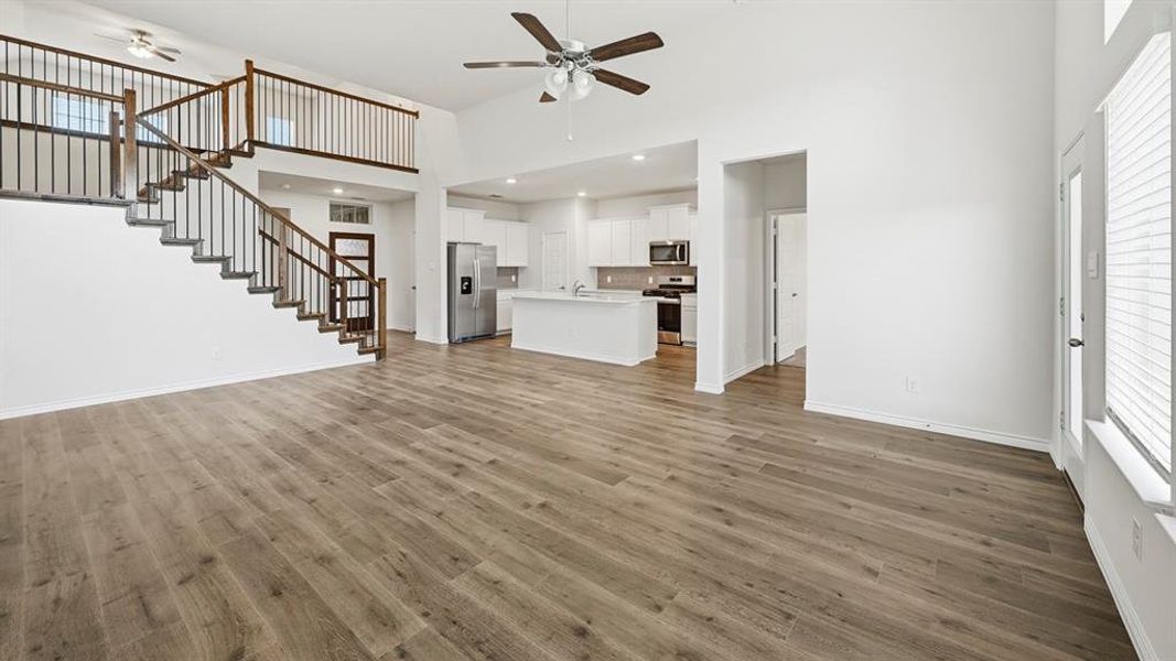 Open-concept living area featuring wood-finish flooring, a two-story ceiling, and a prominent staircase with dark wood railings and black spindles