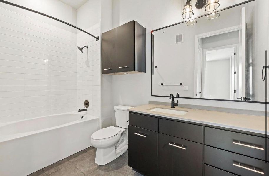 A contemporary vanity with dark cabinetry sits opposite a tiled tub in this modern bathroom. A contemporary vanity with dark cabinetry sits opposite a tiled tub in this modern bathroom.