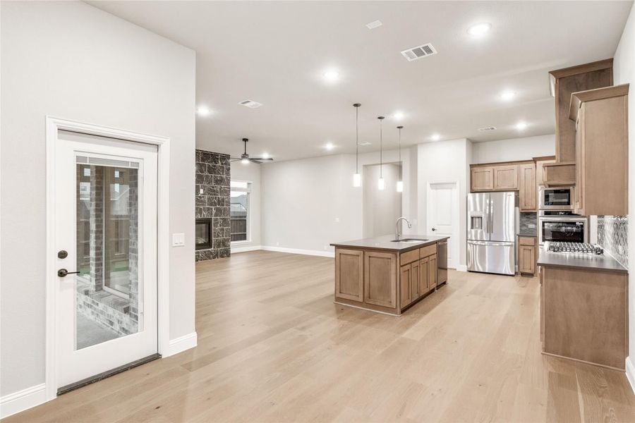 Open-concept kitchen with wood island, stainless appliances, and light hardwood floors opening to living area with stone fireplace