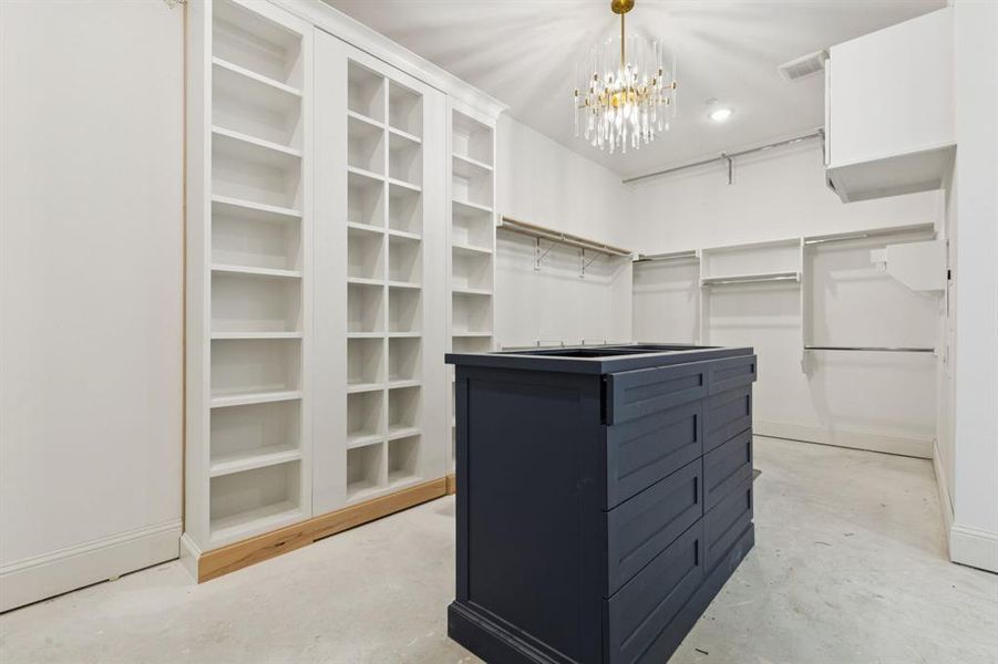 Custom primary closet with second laundry, large center disiplay island, top pull down racks, makeup vanity, and concealed storage room.
