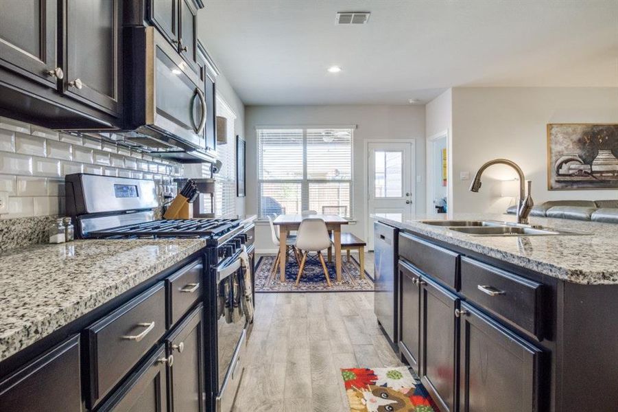 Kitchen with visible vents, decorative backsplash, light wood-style floors, stainless steel appliances, and a sink