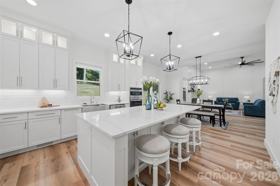 Crisp white custom cabinetry stretches to the ceiling, creating an airy, upscale feel, while the oversized quartz island becomes the perfect gathering place for entertaining, morning coffee, or everyday living