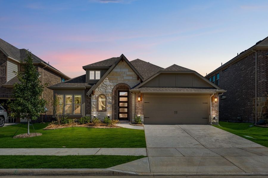 Single-story home with stone and brick exterior, arched entry, two-car garage, and manicured lawn at dusk
