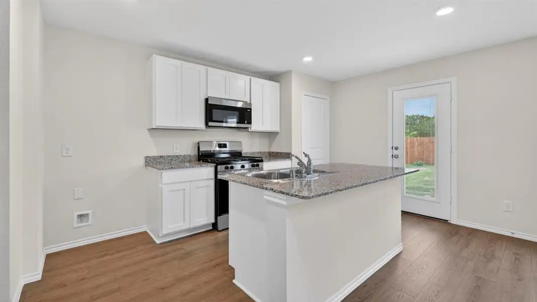 Kitchen featuring an island with a dual-basin stainless steel sink, granite countertops, white cabinetry, and wood-finish flooring